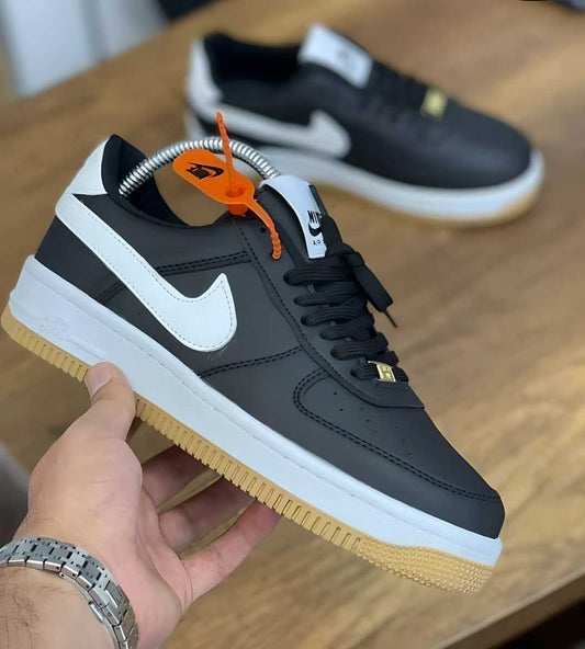 Hand holding black Nike Air Force 1 sneakers with white swoosh and gum sole