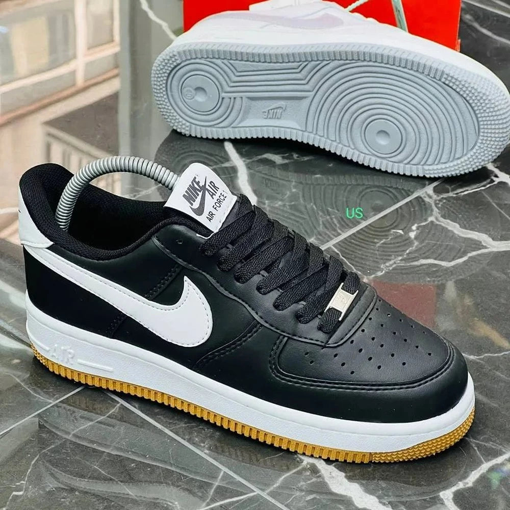 Hand holding black Nike Air Force 1 sneakers with white swoosh and gum sole