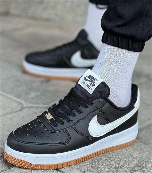 Hand holding black Nike Air Force 1 sneakers with white swoosh and gum sole